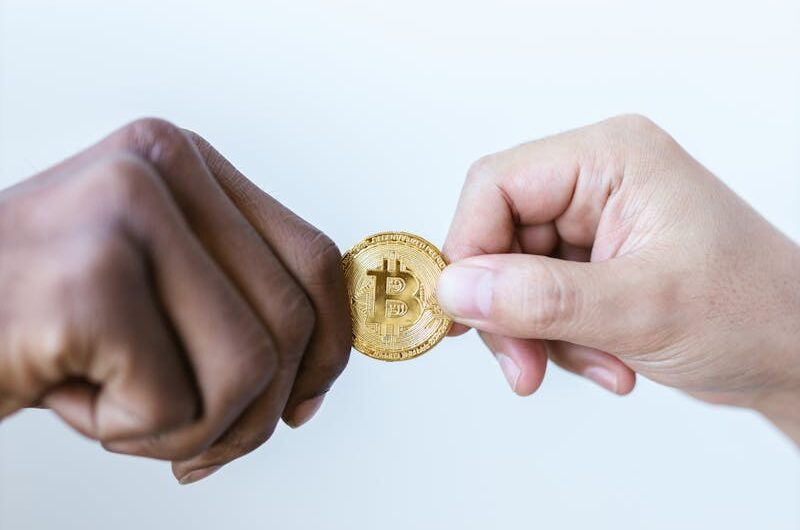 Close-up of two diverse hands exchanging a gold bitcoin coin, symbolizing cryptocurrency trade. - Digital Real Estate in Dubai
