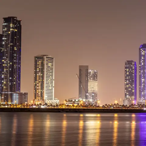 Sharjah DED Implements Fee Reductions and - Stunning night view of Sharjah's modern skyline reflected in calm water.