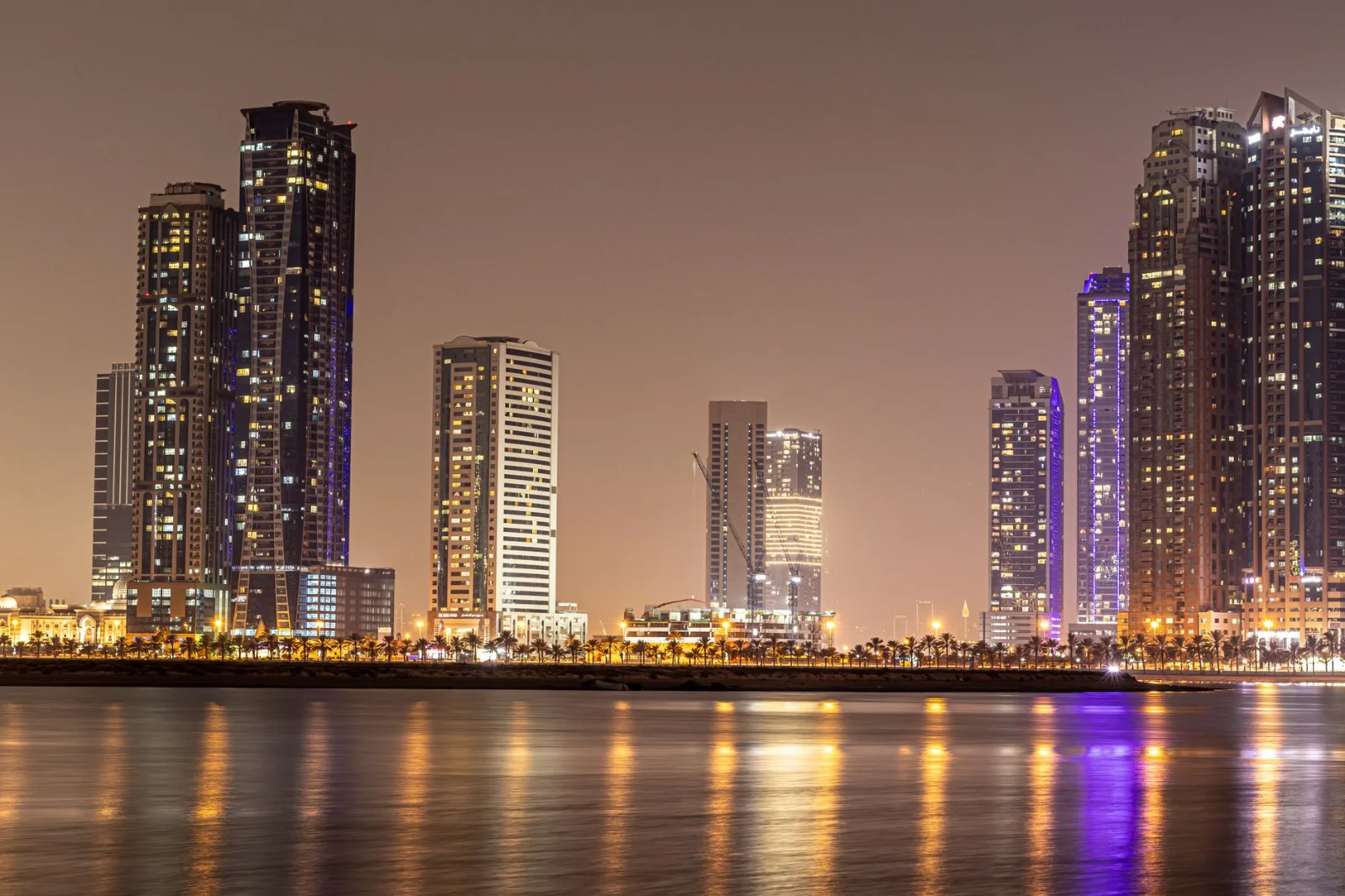 Sharjah DED Implements Fee Reductions and - Stunning night view of Sharjah's modern skyline reflected in calm water.