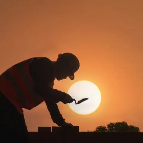 UAE Midday Work Ban 2026: Mandatory - A construction worker's silhouette against a vibrant sunset sky, symbolizing hard work