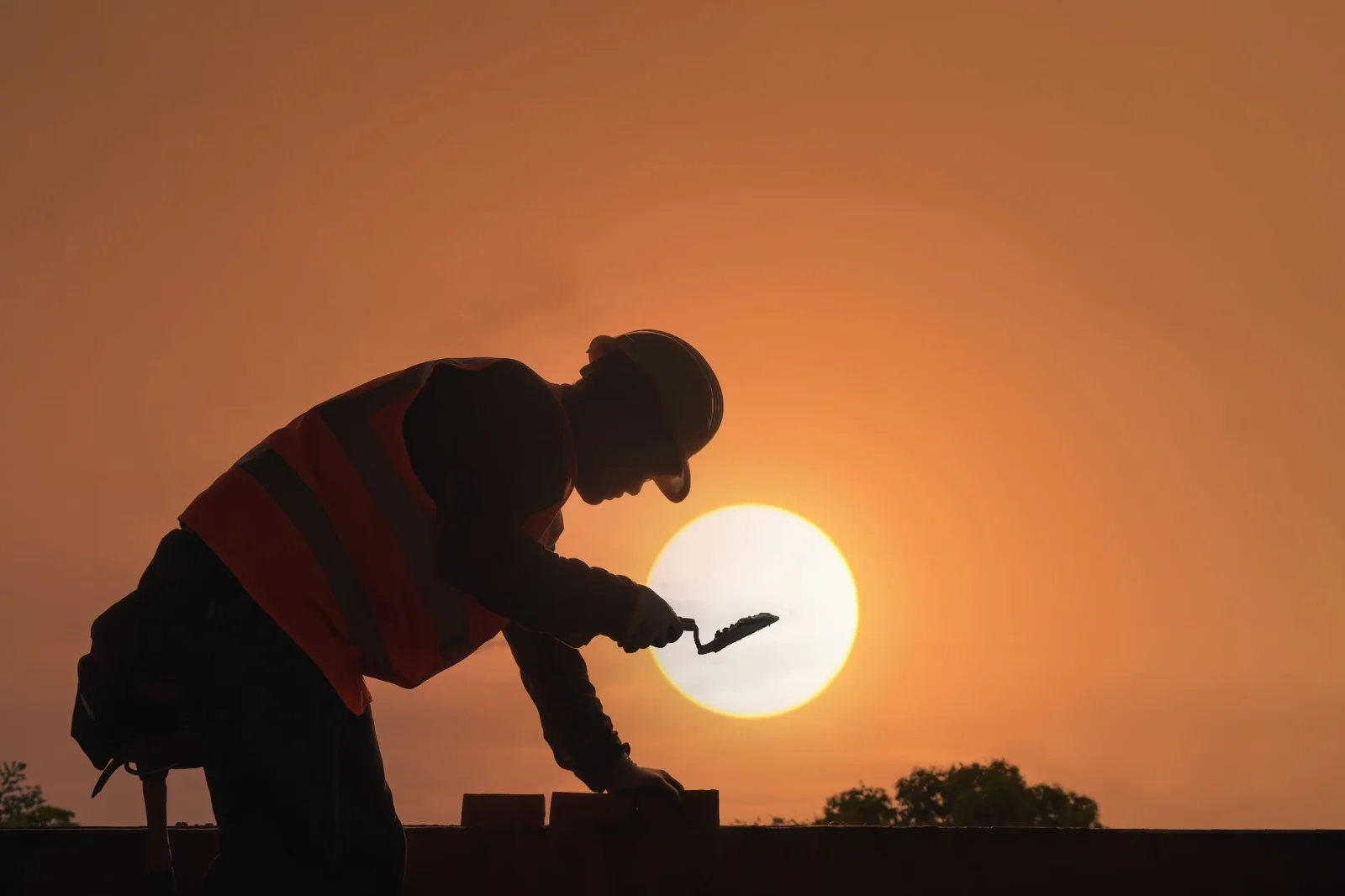 UAE Midday Work Ban 2026: Mandatory - A construction worker's silhouette against a vibrant sunset sky, symbolizing hard work